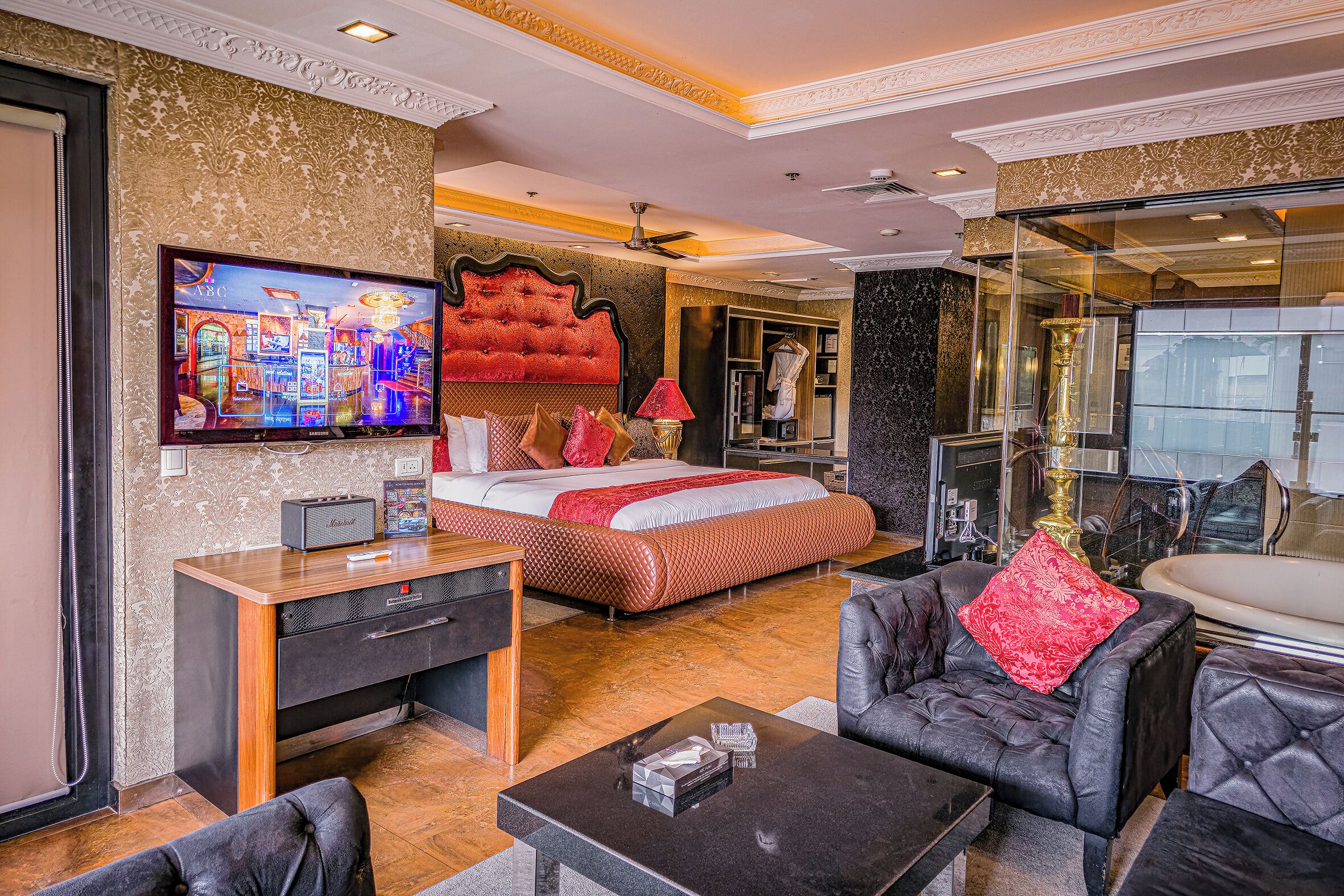 A modern hotel room with a large bed, a TV, a desk, and a seating area.