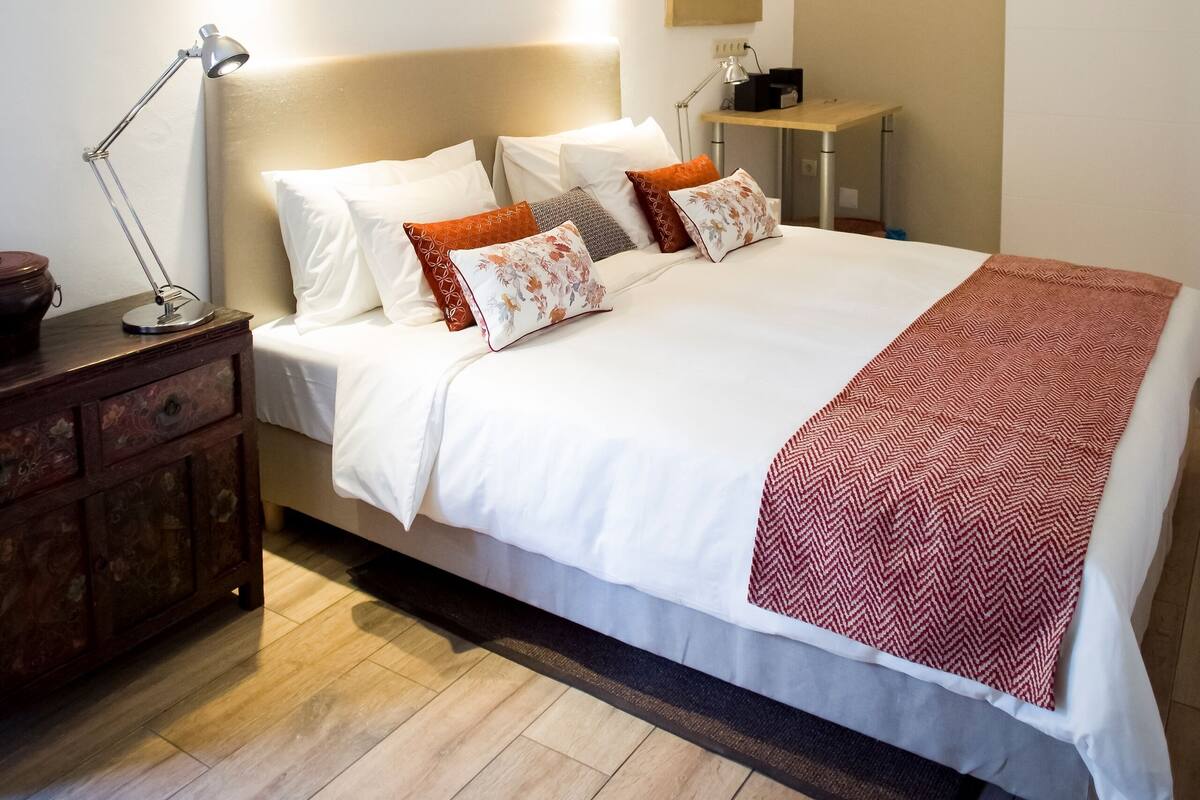 A neatly arranged bedroom with a bed, bedside tables, a desk, and a wall-mounted shelf.