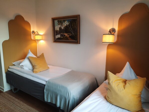 A hotel room with two beds, each with a headboard, a painting on the wall, and two wall-mounted lamps. - Hotel Lysekil (Lysekil)