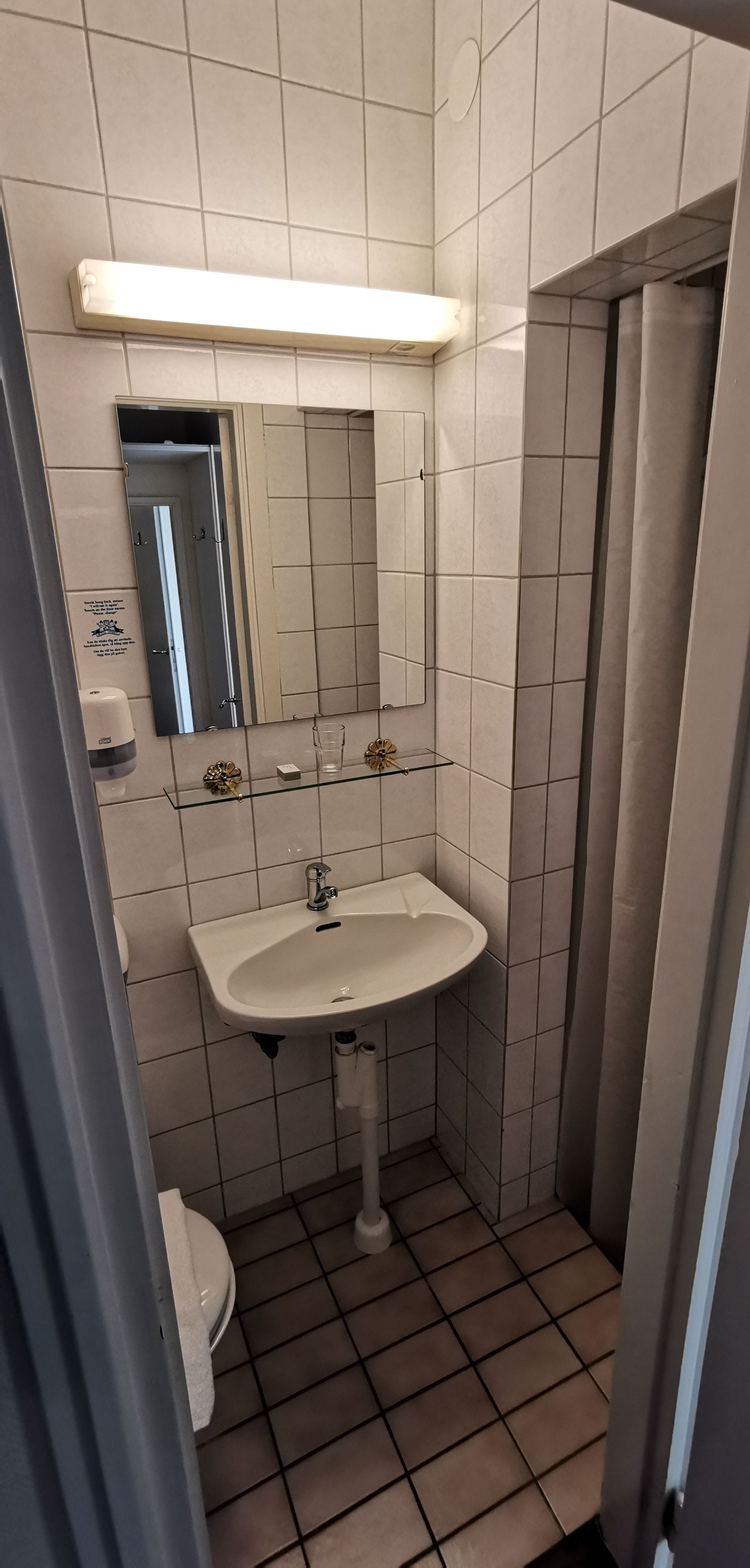 A small, tiled bathroom with a white sink, a mirror, and a shower stall.