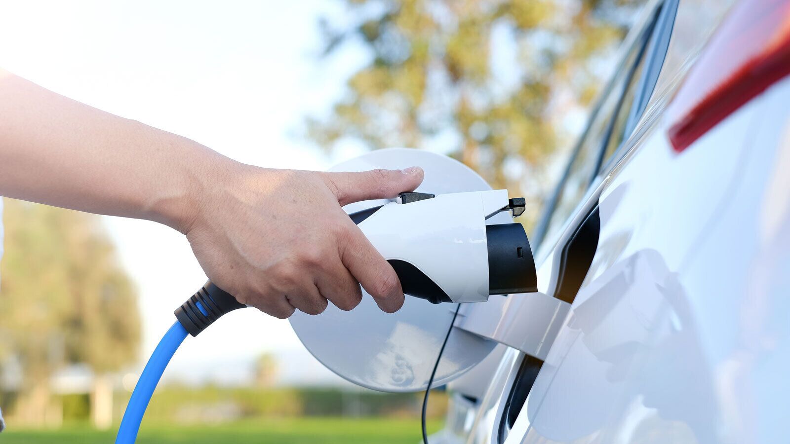 Käsi kytkee sähköauton latauskaapelin autoon.