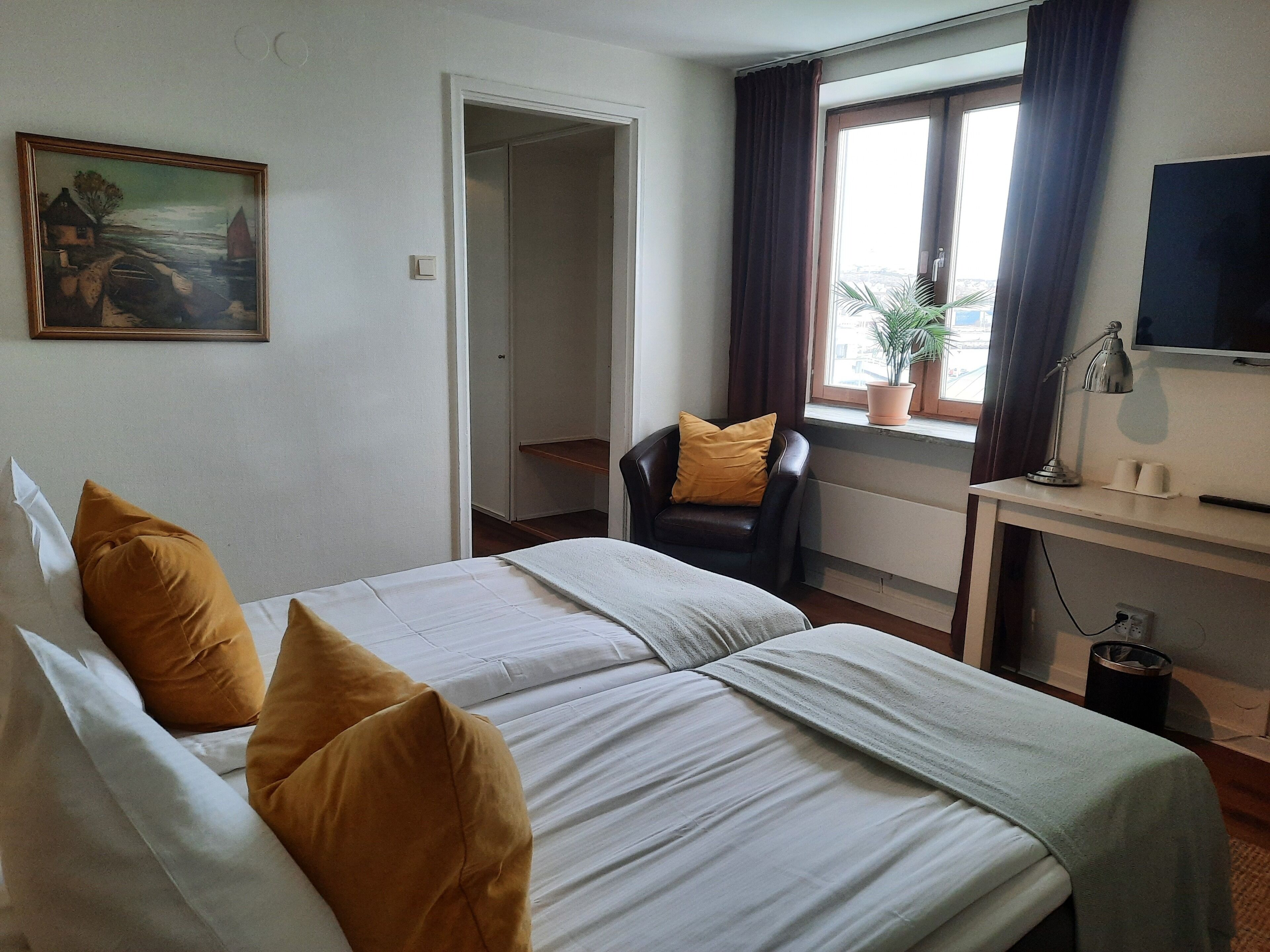 Habitación de hotel con cama, escritorio, silla, televisor y ventana con cortinas.