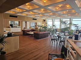 Amplia sala de estar con piso de madera, un sofá de cuero marrón, una mesa de comedor con sillas y una zona de cocina con mostrador y armarios.