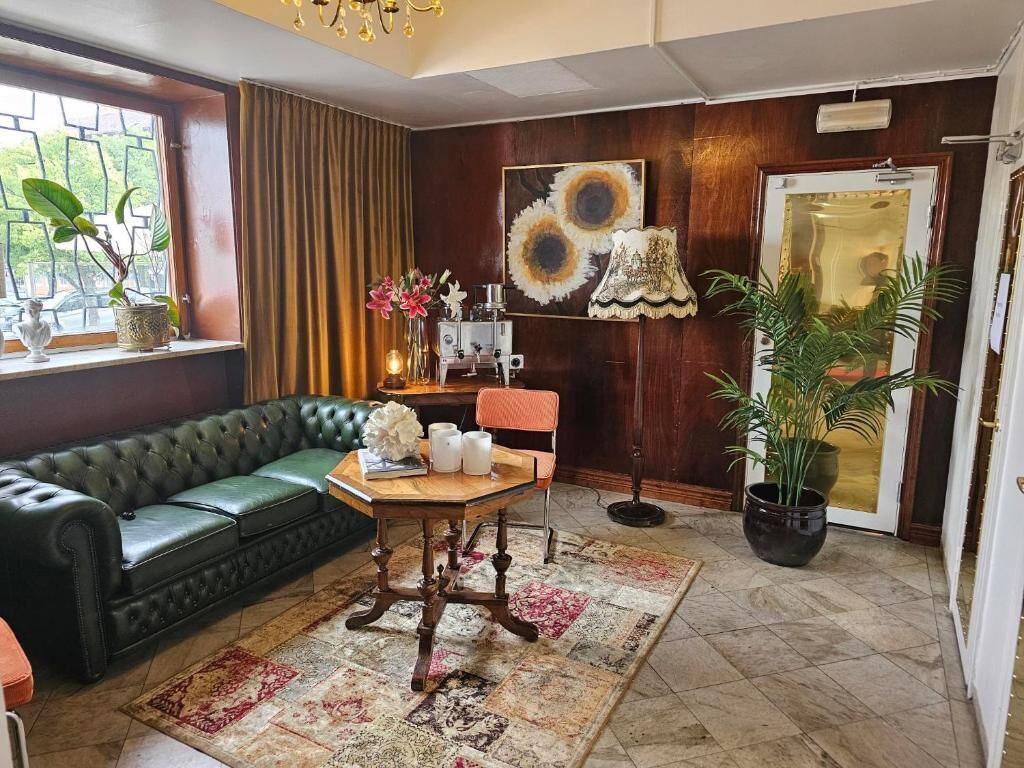 A living room with a green leather sofa, a wooden dining table with candles, a patterned rug, and a large potted plant.