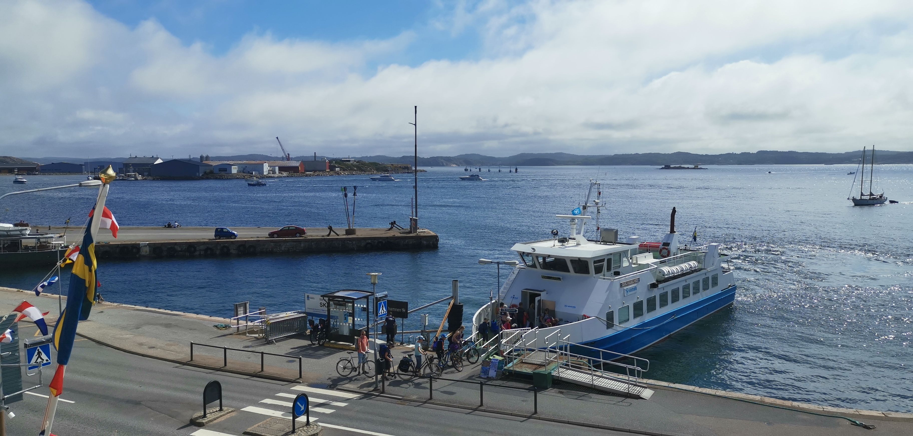 A ferry dock with a boat, a pedestrian walkway, and a clear view of the water and distant hills.