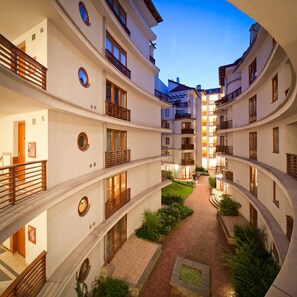 Un immeuble résidentiel à plusieurs étages, doté de balcons, d’une cour intérieure et d’un chemin bordé de briques.