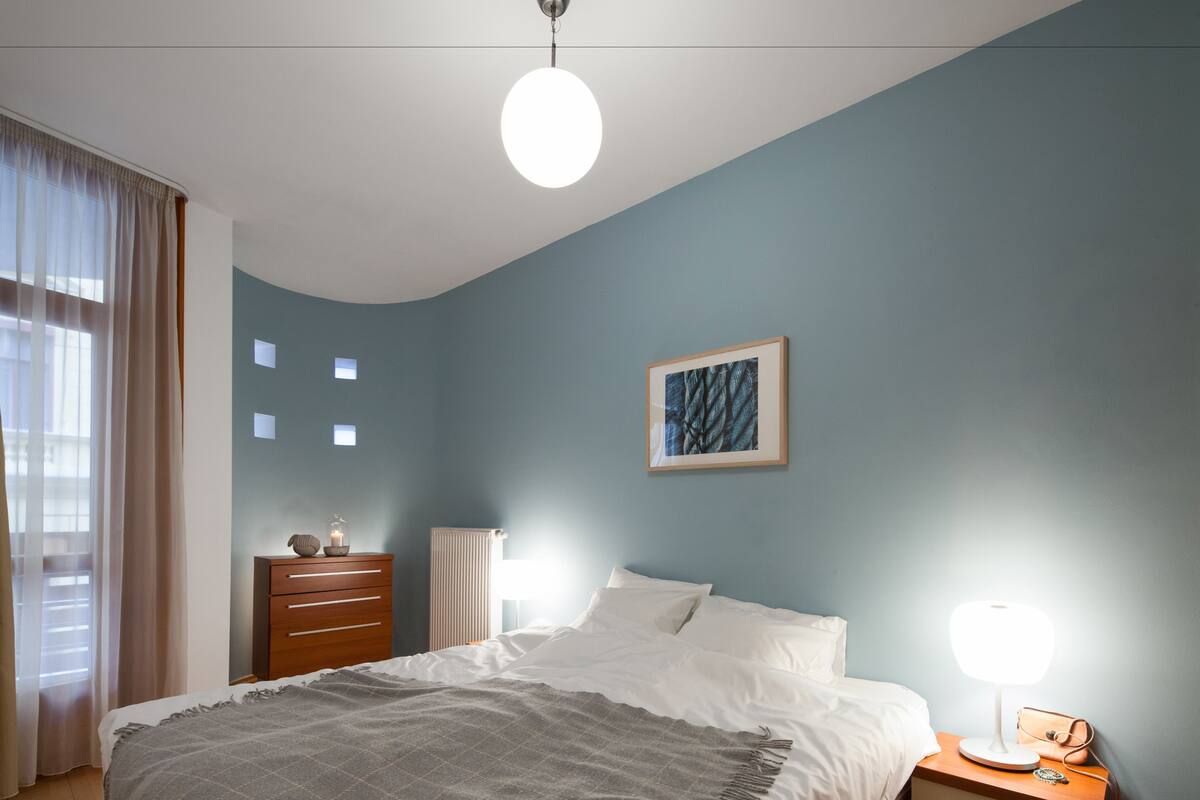 A bedroom with a bed, bedside table, and a wall-mounted light fixture.