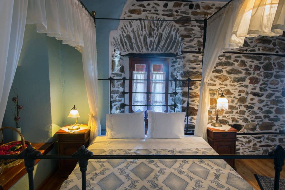 Un dormitorio con pared de piedra, una ventana con cortinas, una cama con colcha estampada y dos lámparas de noche.