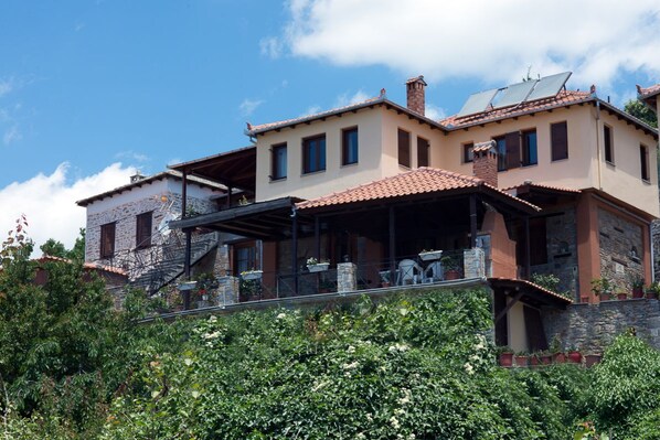 Un immeuble à plusieurs étages doté d’une terrasse, de murs en pierre et de panneaux solaires.