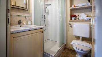 Un bagno con cabina doccia in vetro, un lavabo con piano in marmo e un water con un asciugamano sopra.