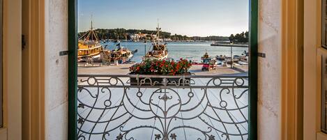 A balcony with a wrought iron railing overlooking a marina with boats and a distant shoreline.