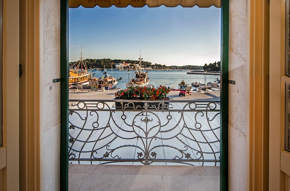 A balcony with a wrought iron railing overlooking a marina with boats and a distant shoreline.