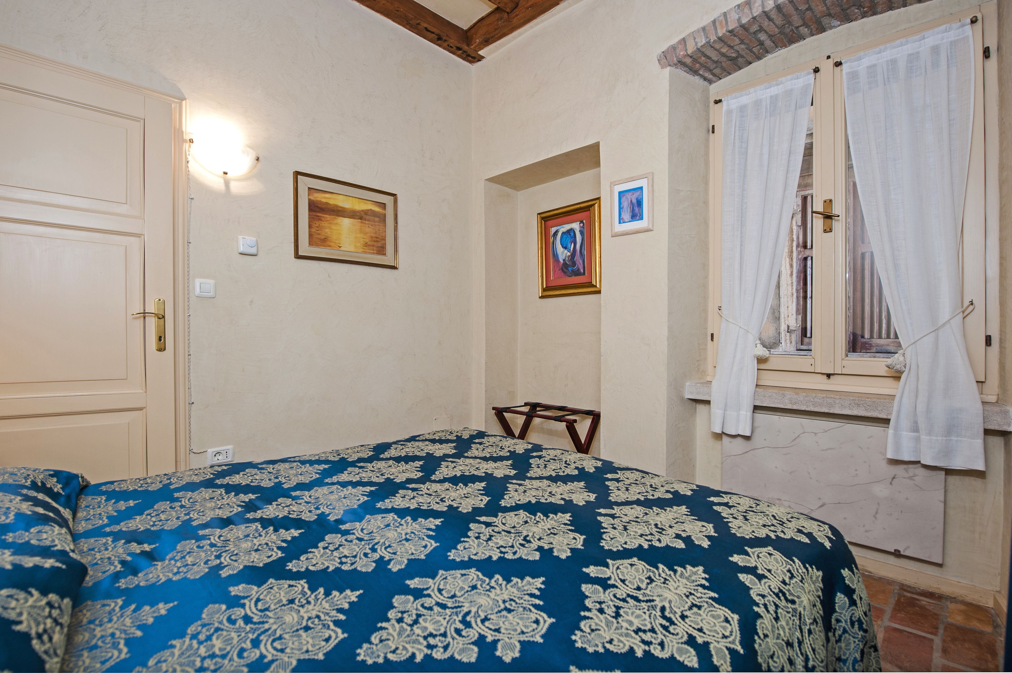 Een slaapkamer met een bed, een deur, een raam met gordijnen en twee ingelijste foto's aan de muur.
