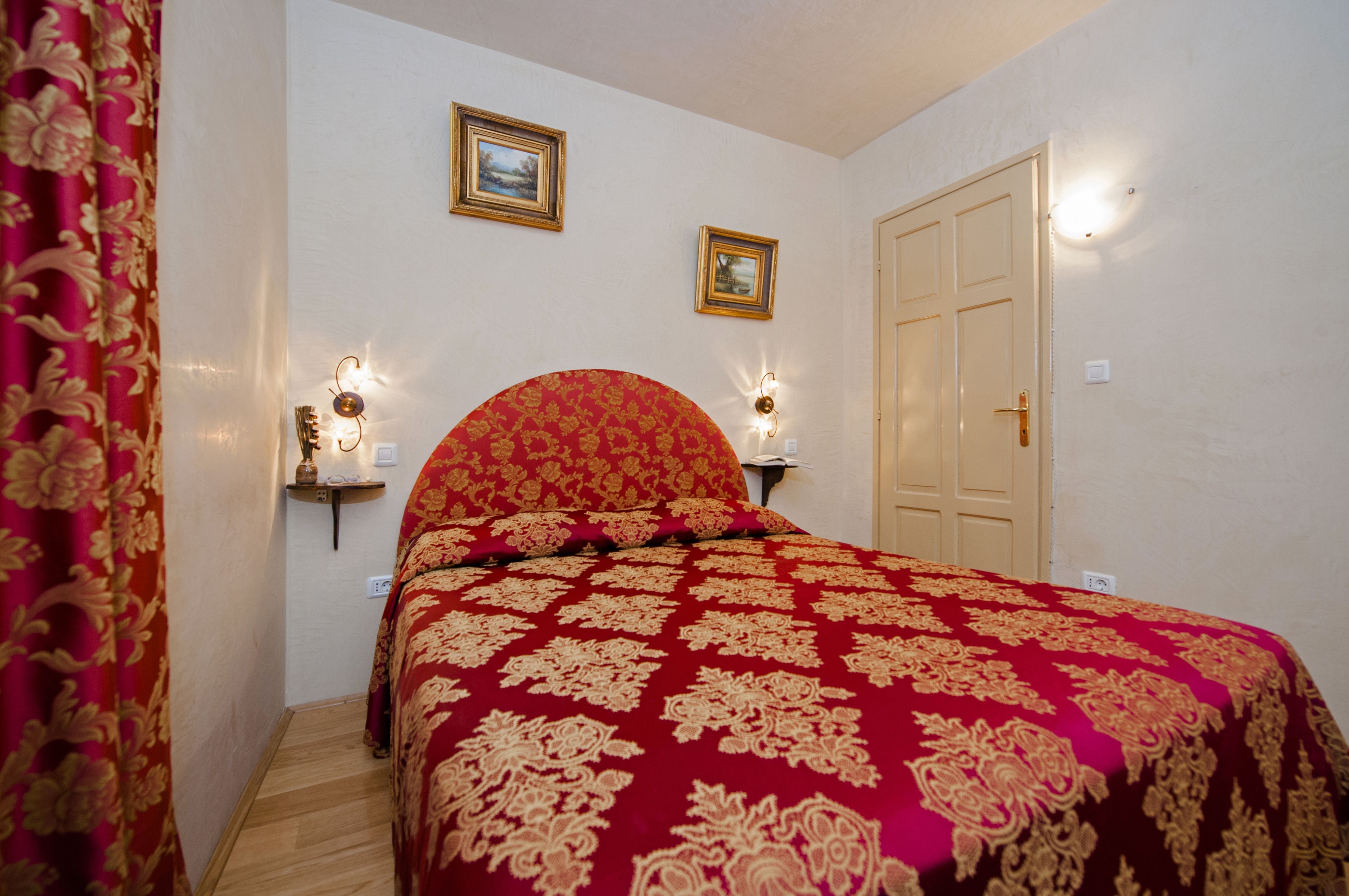 A bedroom with a large bed, two wall-mounted lamps, and two framed pictures.