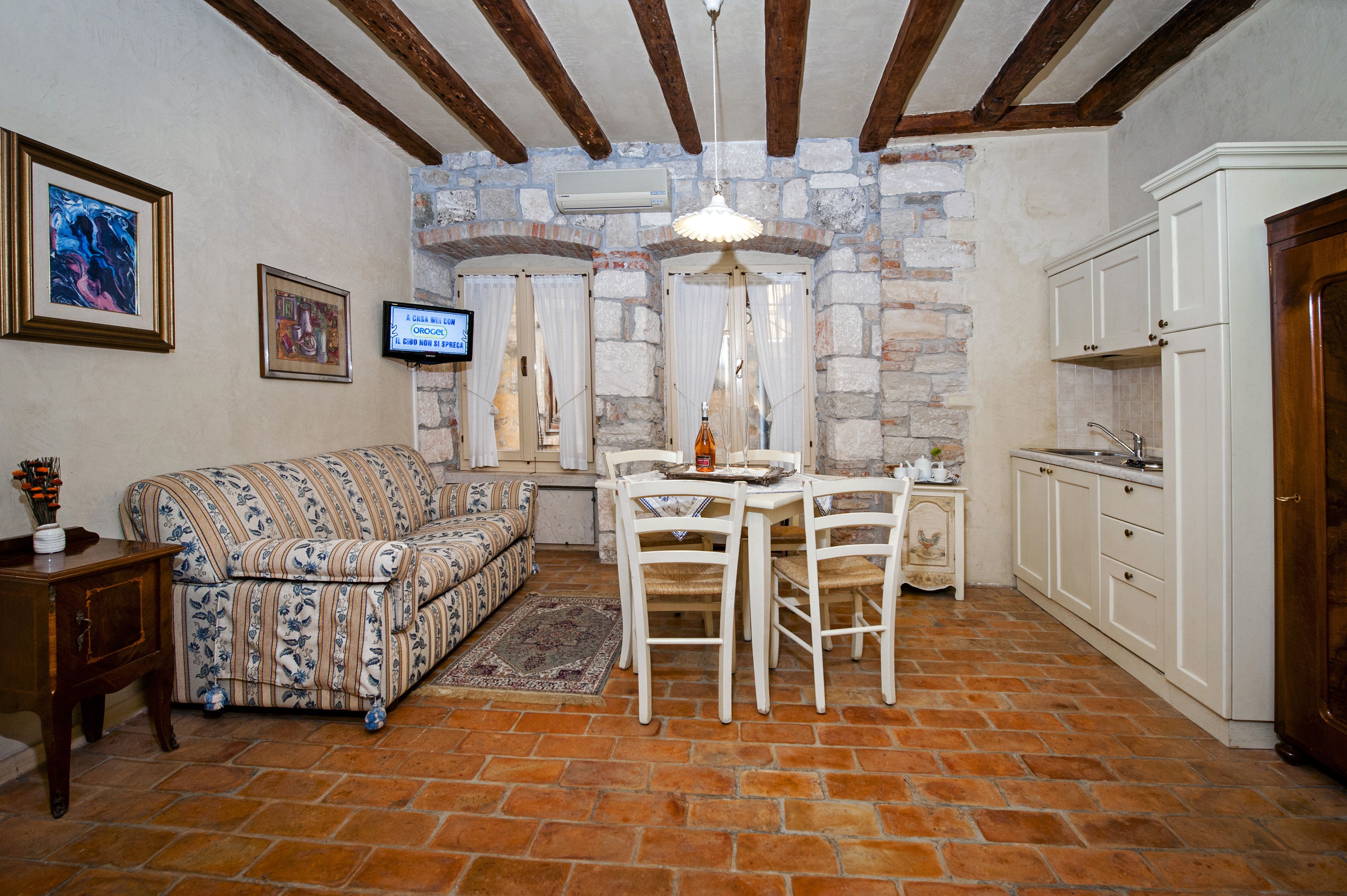 A cozy living room with a patterned sofa, a dining table with chairs, a small side table, and a kitchen area with cabinets and a sink.