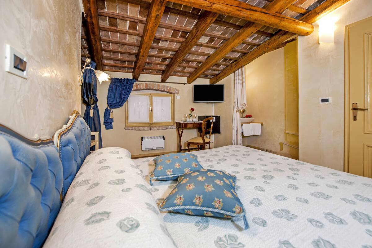 Un dormitorio con techo de madera, una cama con ropa de cama floral, un televisor y una pequeña mesa con una silla.