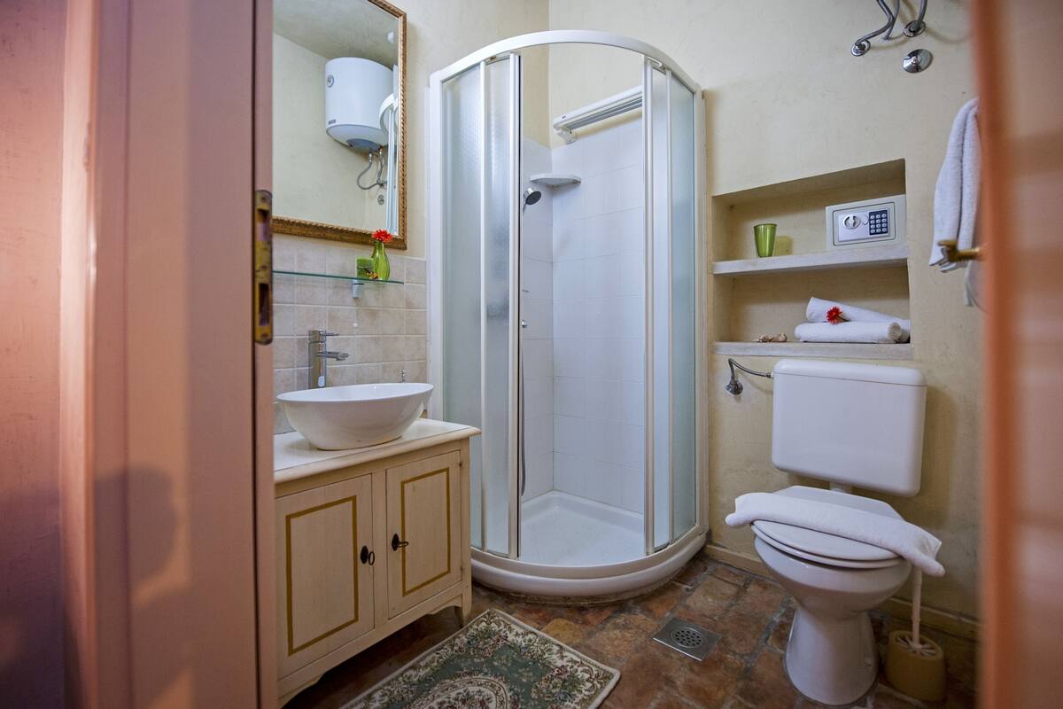 Un baño con ducha, lavamanos, inodoro y espejo.