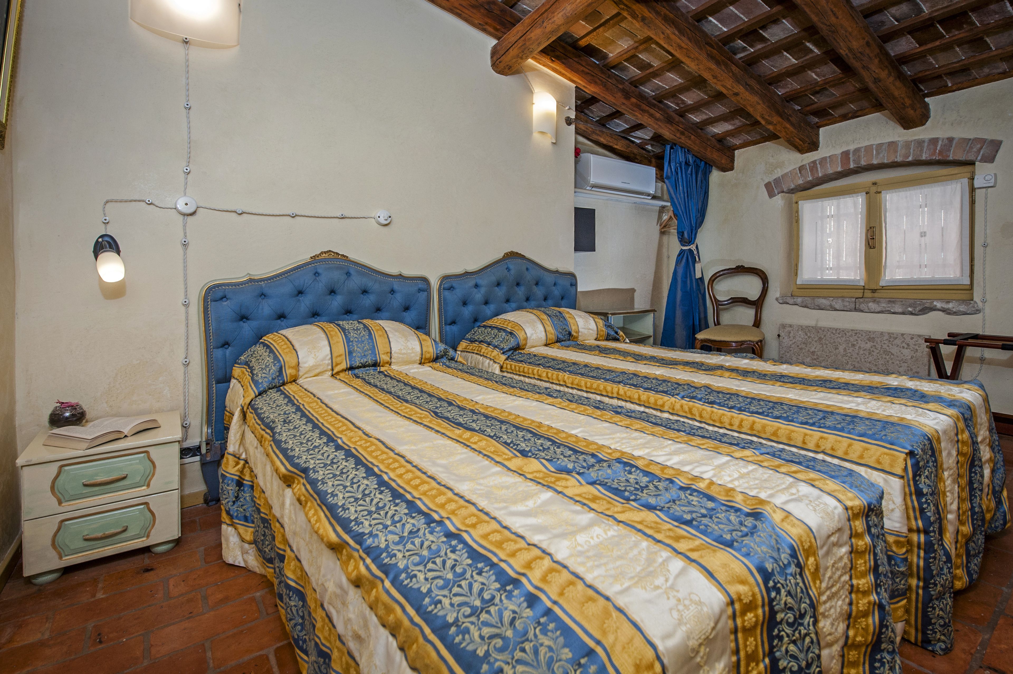 A bedroom with two beds, a nightstand, a lamp, and a window with curtains.