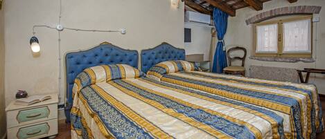 A bedroom with two beds, a nightstand, a lamp, and a window with curtains.