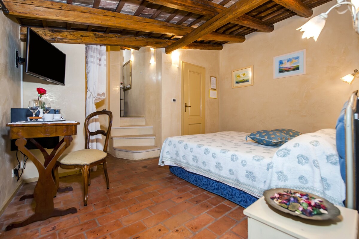 A room with a bed, a desk with a computer, a chair, a TV, and a staircase.