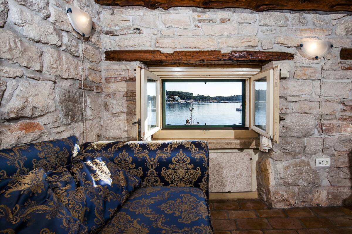 Una habitación con paredes de piedra y ventana con vista al agua.