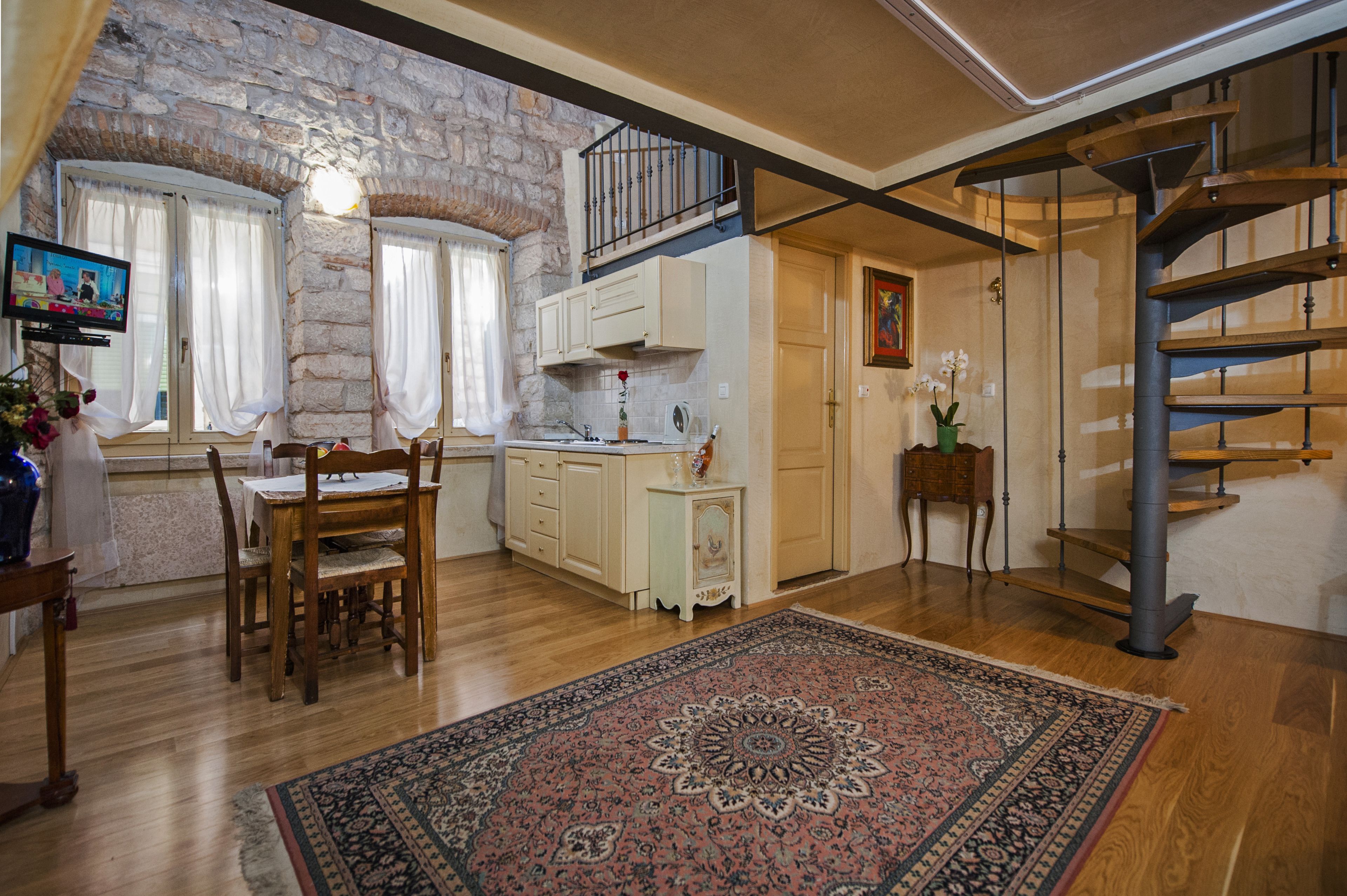 Una cocina amplia con armarios de madera, un comedor con mesa y sillas, una pared de piedra y una escalera de caracol.