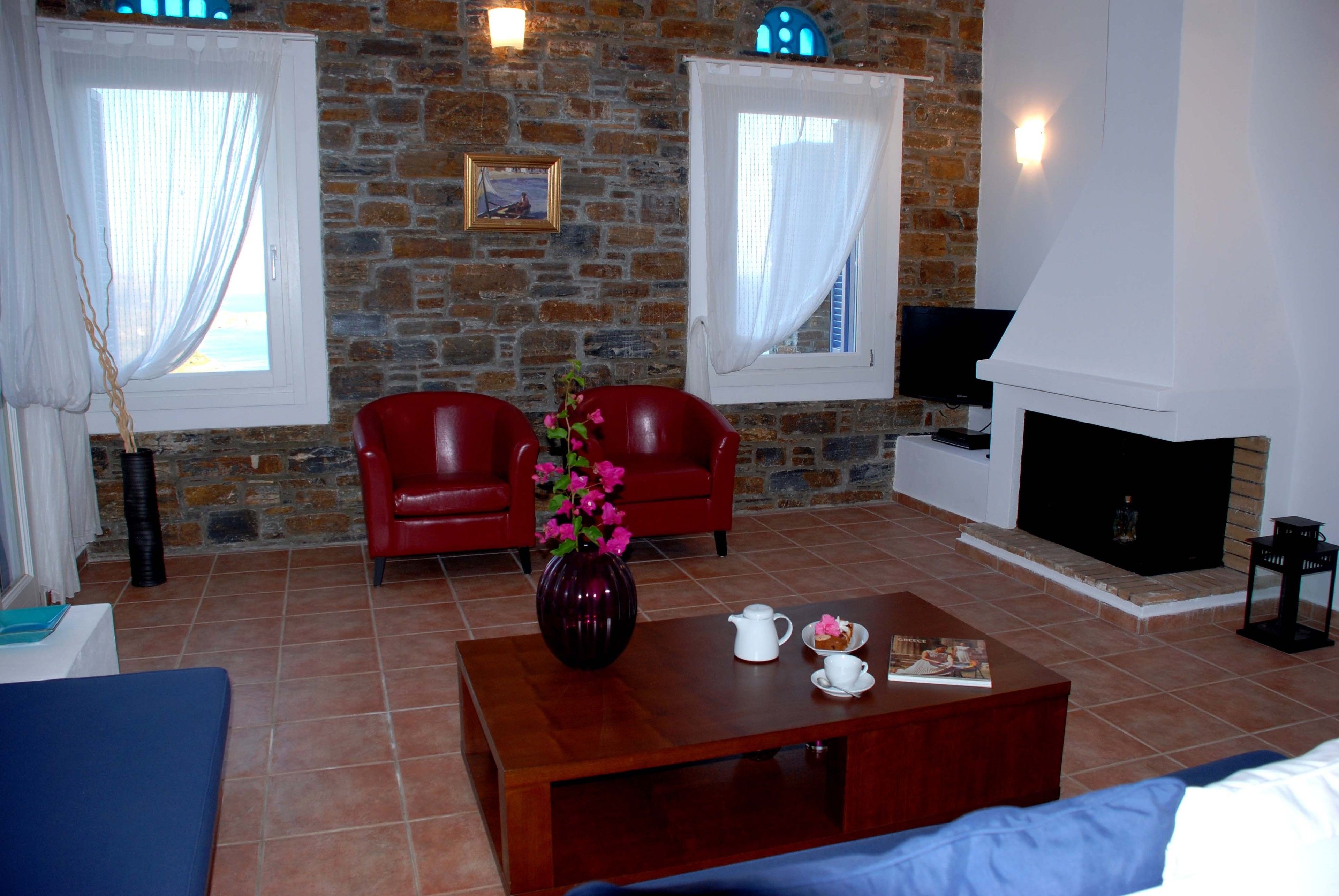 A living room with a stone wall, two red leather chairs, a coffee table with a vase and a book, and a fireplace.