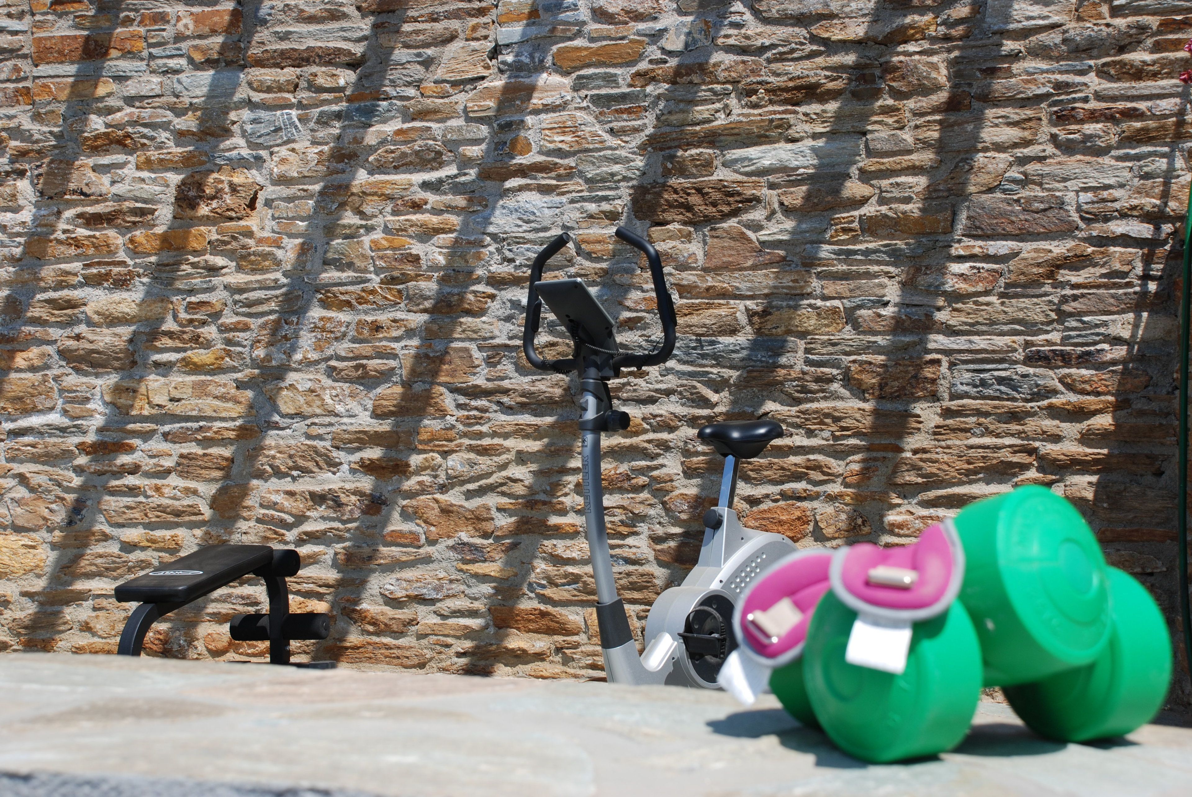 A stone wall with a stationary exercise bike and a bench.