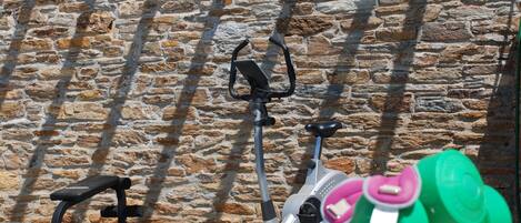 A stone wall with a stationary exercise bike and a bench.