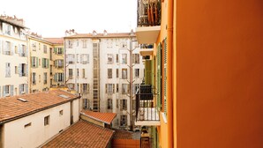 A narrow street between buildings with balconies, a tiled roof, and a visible staircase. - Simple Stay - Fresh Start May 2026 (Nice)