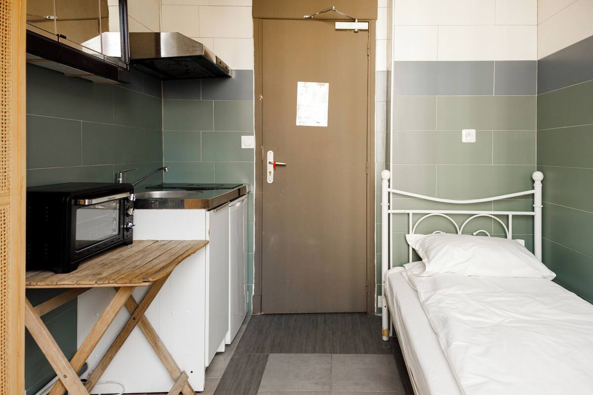 Ein kleines Zimmer mit einer Küchenzeile, einem Bett und einer Tür.
