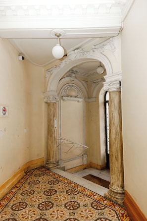 An interior hallway with ornate columns, a patterned floor, and a ceiling light fixture. - Simple Stay - Fresh Start May 2026 (Nice)