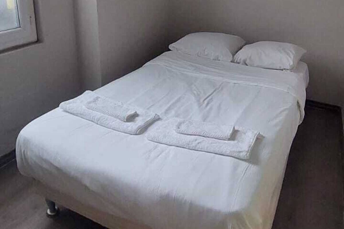 Ein Einzelbett mit weißer Bettwäsche in einem Zimmer mit Fenster und schlichter Wand.