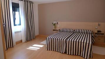 Un dormitorio con cama, mesita de noche, planta y ventana con cortinas.
