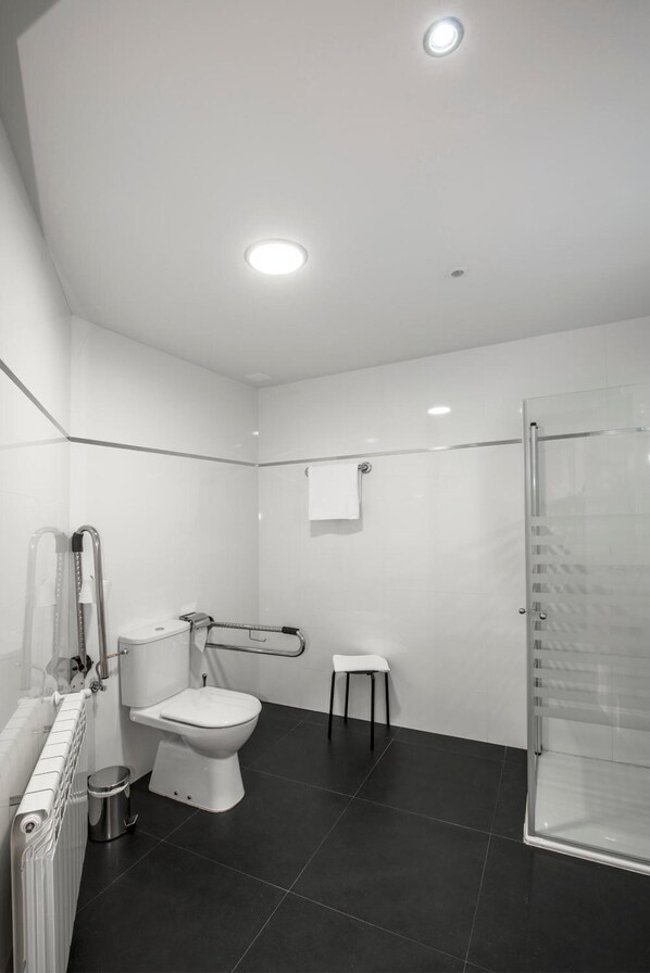 Un baño moderno con inodoro, cabina de ducha de vidrio, un taburete pequeño y un perchero para toallas.