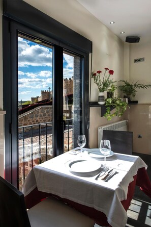 Mesa puesta con platos, cubiertos y vasos, con vista a un castillo a través de un ventanal.