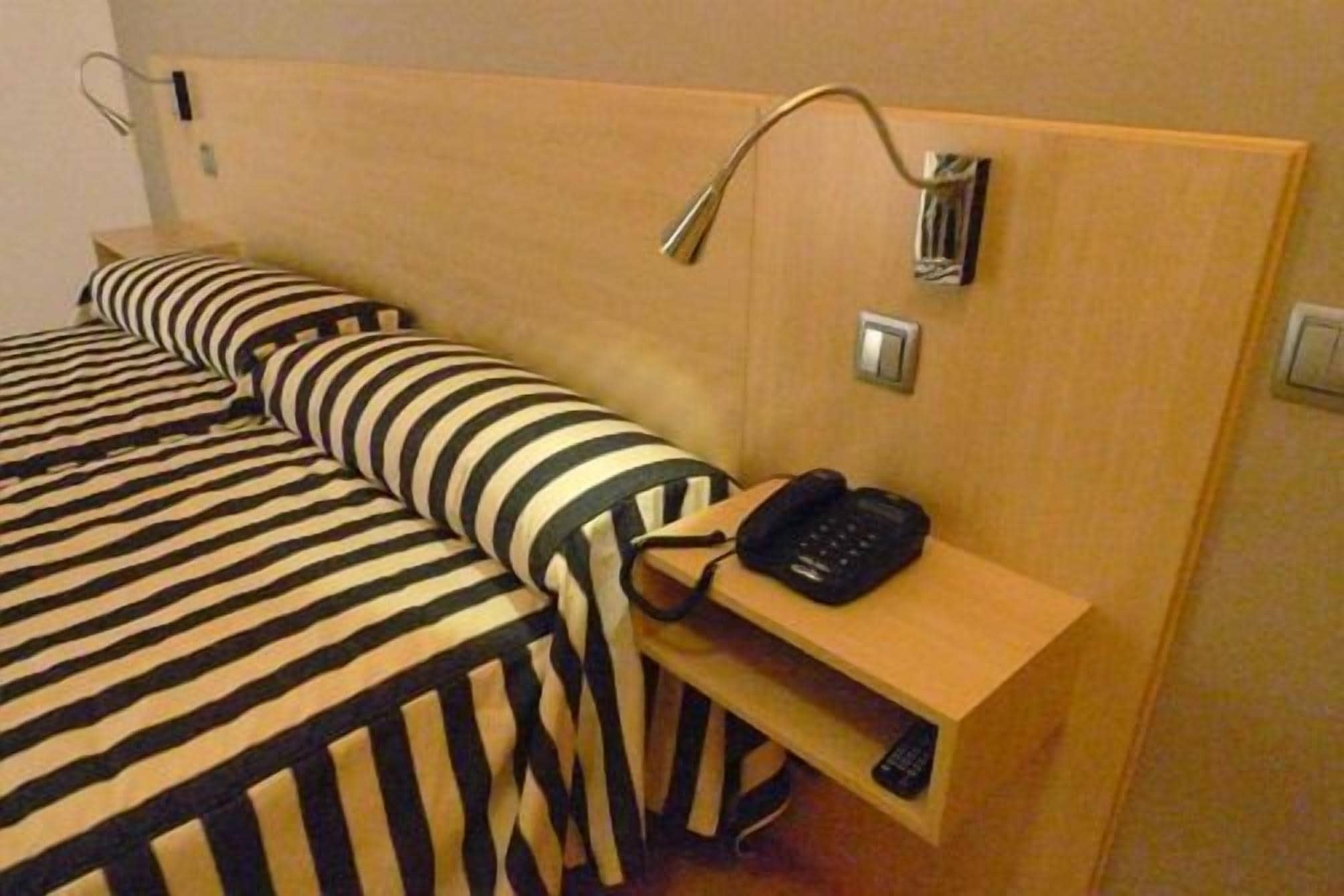 A hotel room with a wooden headboard, a bedside table with a telephone, and striped bedding.