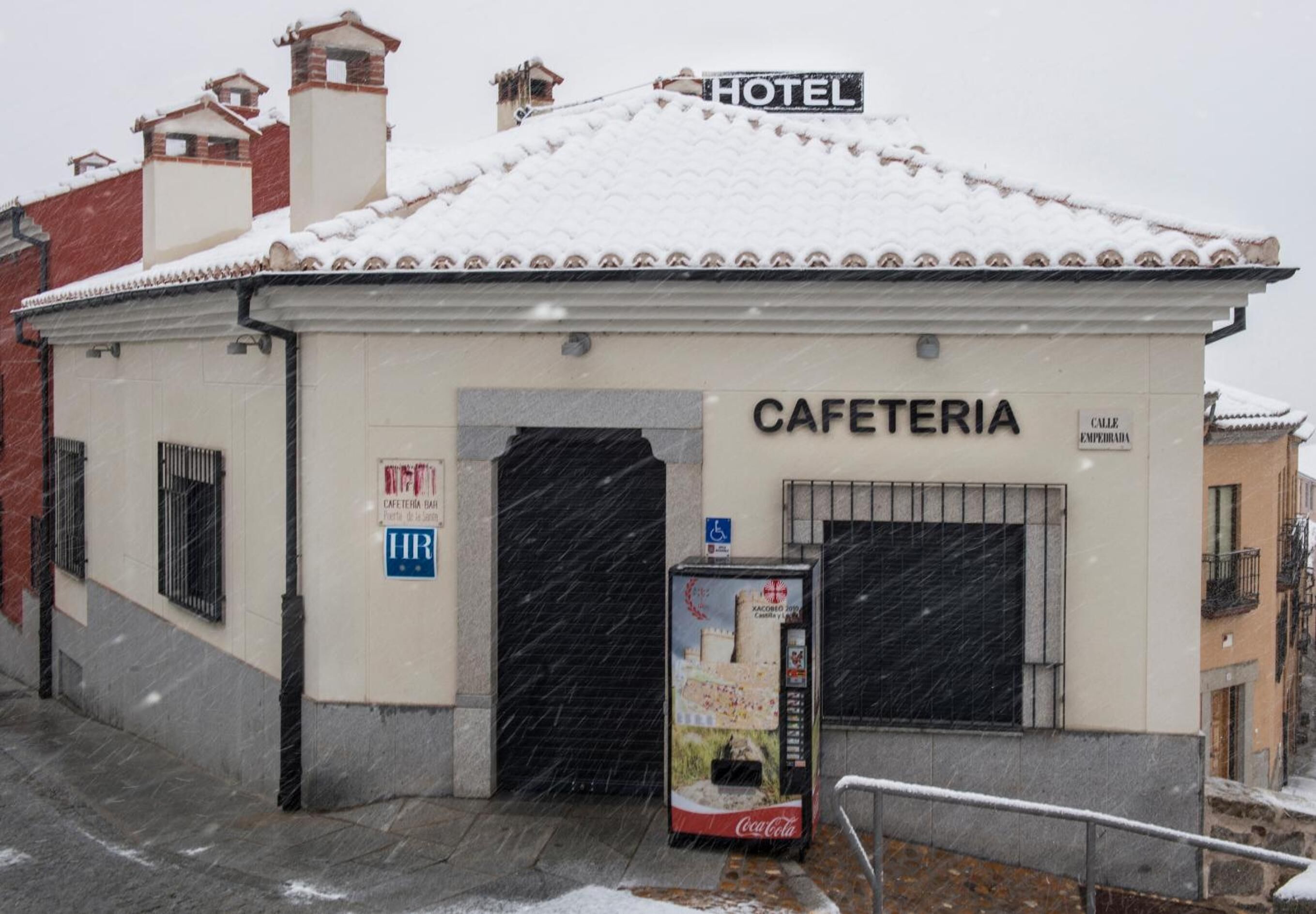 A hotel with a sign reading "HOTEL" and a "CAFETERIA" sign. There is a Coca-Cola vending machine in front.