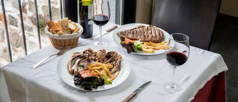 Una mesa dispuesta con comida que incluye bistec, papas fritas y ensalada, con copas de vino y una botella.