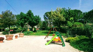 A playground with a swing set and climbing structure, surrounded by potted plants and trees. - Terra dei Santi Country House (Spello)