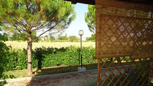 A patio area with a pergola, a stone pathway, and a view of a garden with a tree and a lamp post. - Terra dei Santi Country House (Spello)