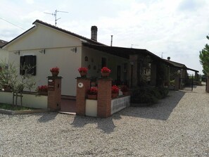 Une maison à deux étages avec une allée en gravier, des piliers en briques ornés de fleurs rouges et un porche abrité.