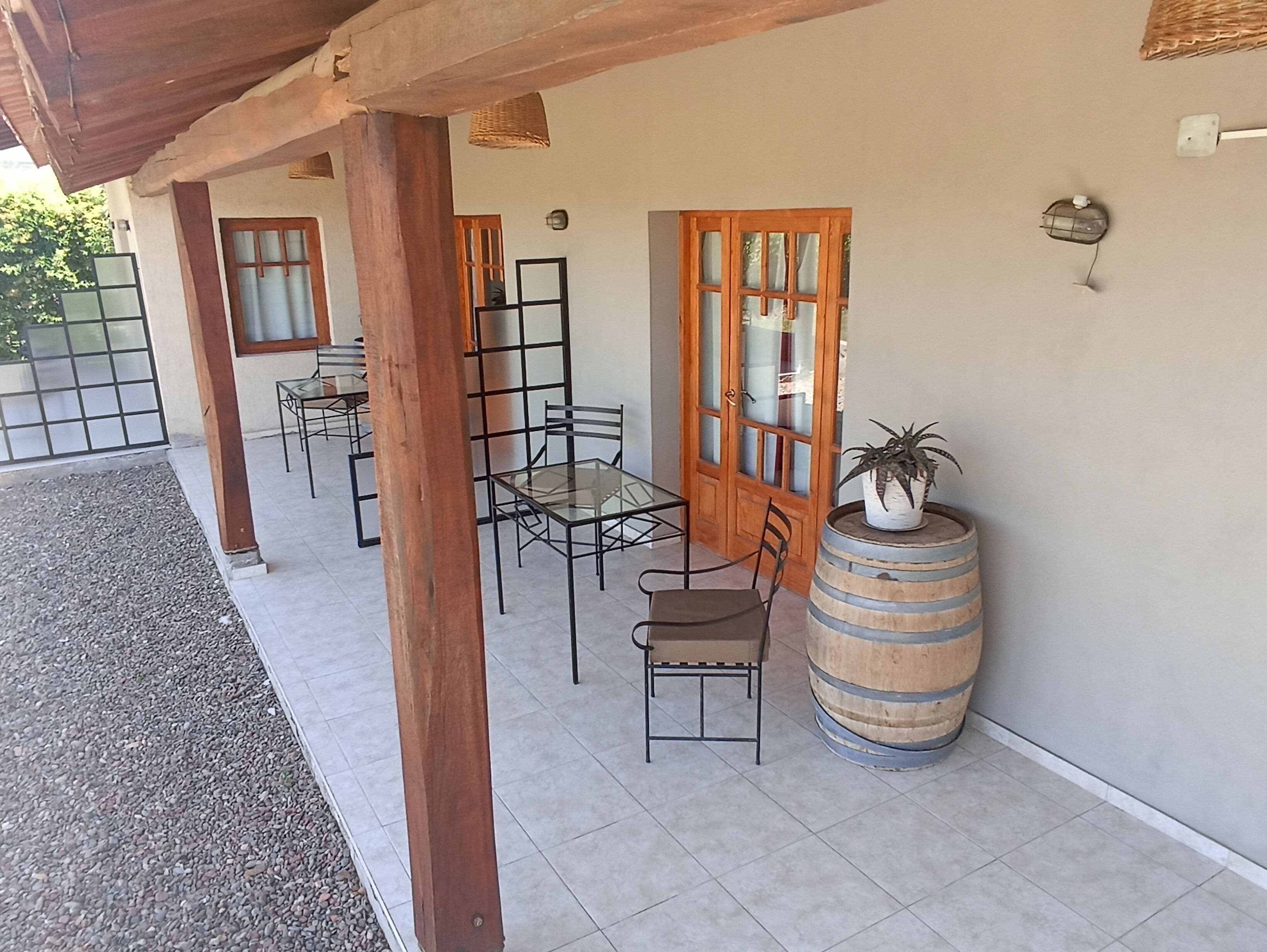 An outdoor patio with a table and chairs, wooden columns, a potted plant, and a barrel.
