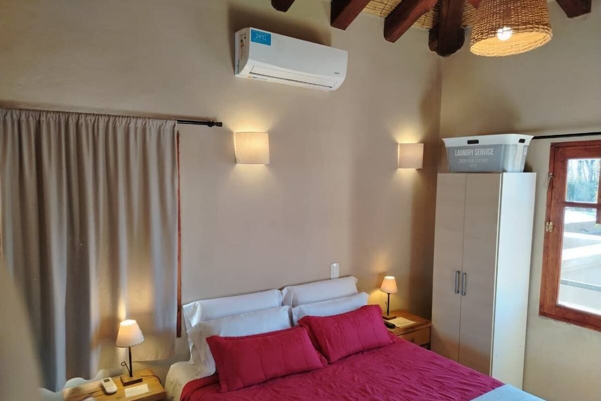 A bedroom with a bed, two bedside lamps, a wardrobe, an air conditioning unit, and a laundry service box.