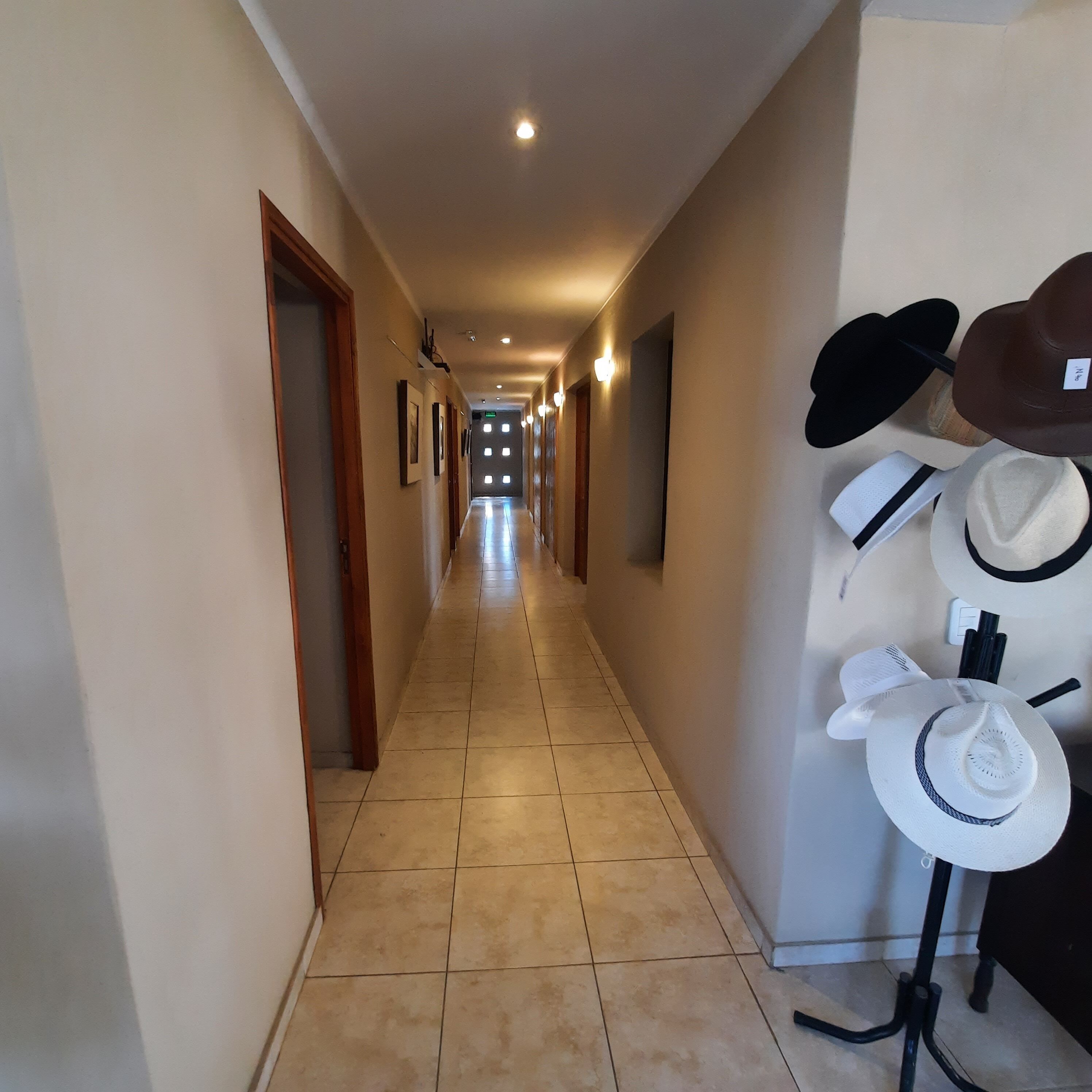 A hotel corridor with a tiled floor, wooden doors, and a wall-mounted hat rack with various hats.