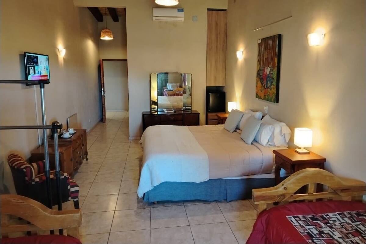 A bedroom with a large bed, a wooden headboard, a bedside table with a lamp, a dresser, a mirror, and a television.