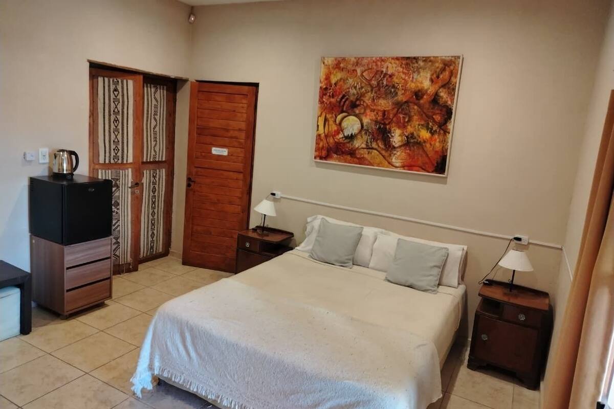 A bedroom with a bed, two bedside tables, a nightstand, a wardrobe, and a painting on the wall.