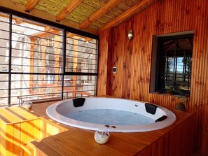 Une cabane en bois dotée d’un bain à remous, de grandes fenêtres et d’une terrasse en bois.