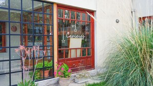 Un edificio con puerta roja y ventanas amplias, un cartel que dice "Cavieres Posada" y plantas en macetas al frente.