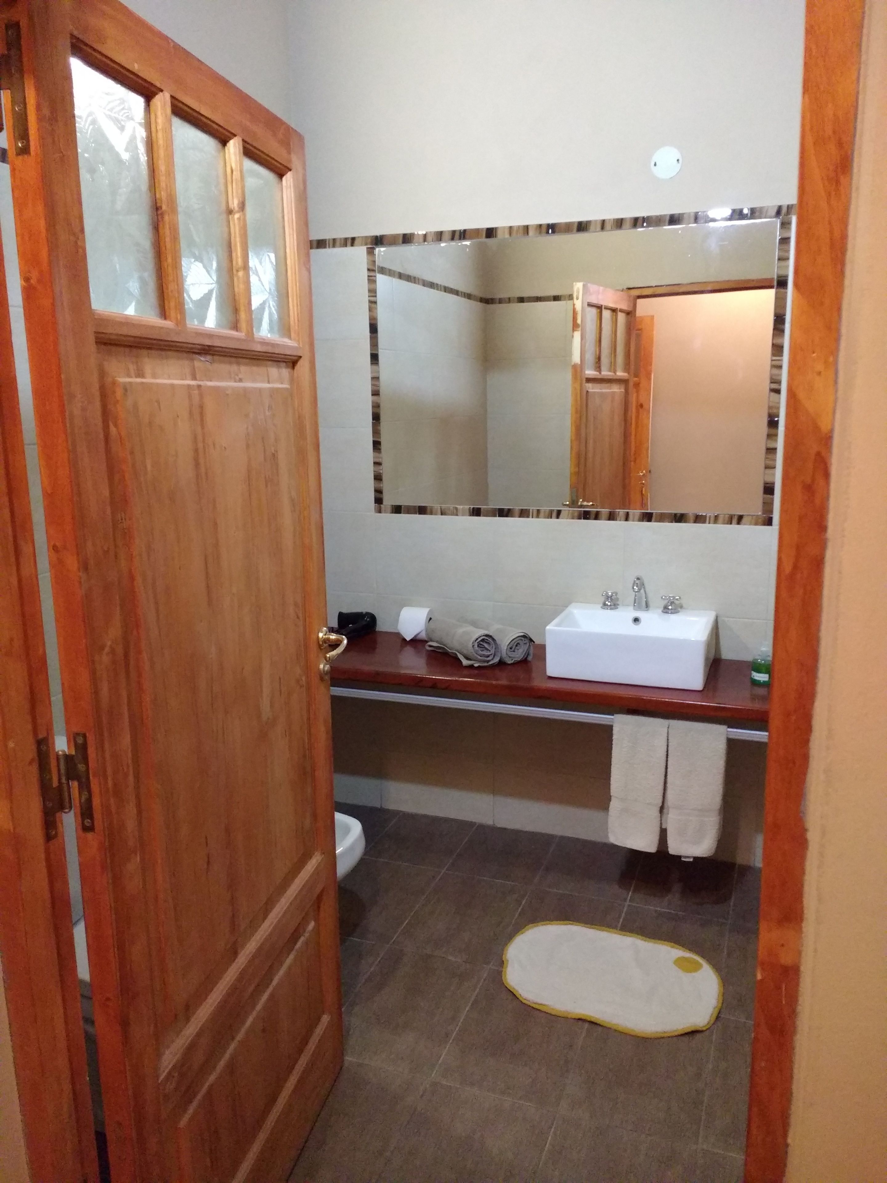 A bathroom with a wooden door, a white sink, a mirror, and a small rug on the floor.